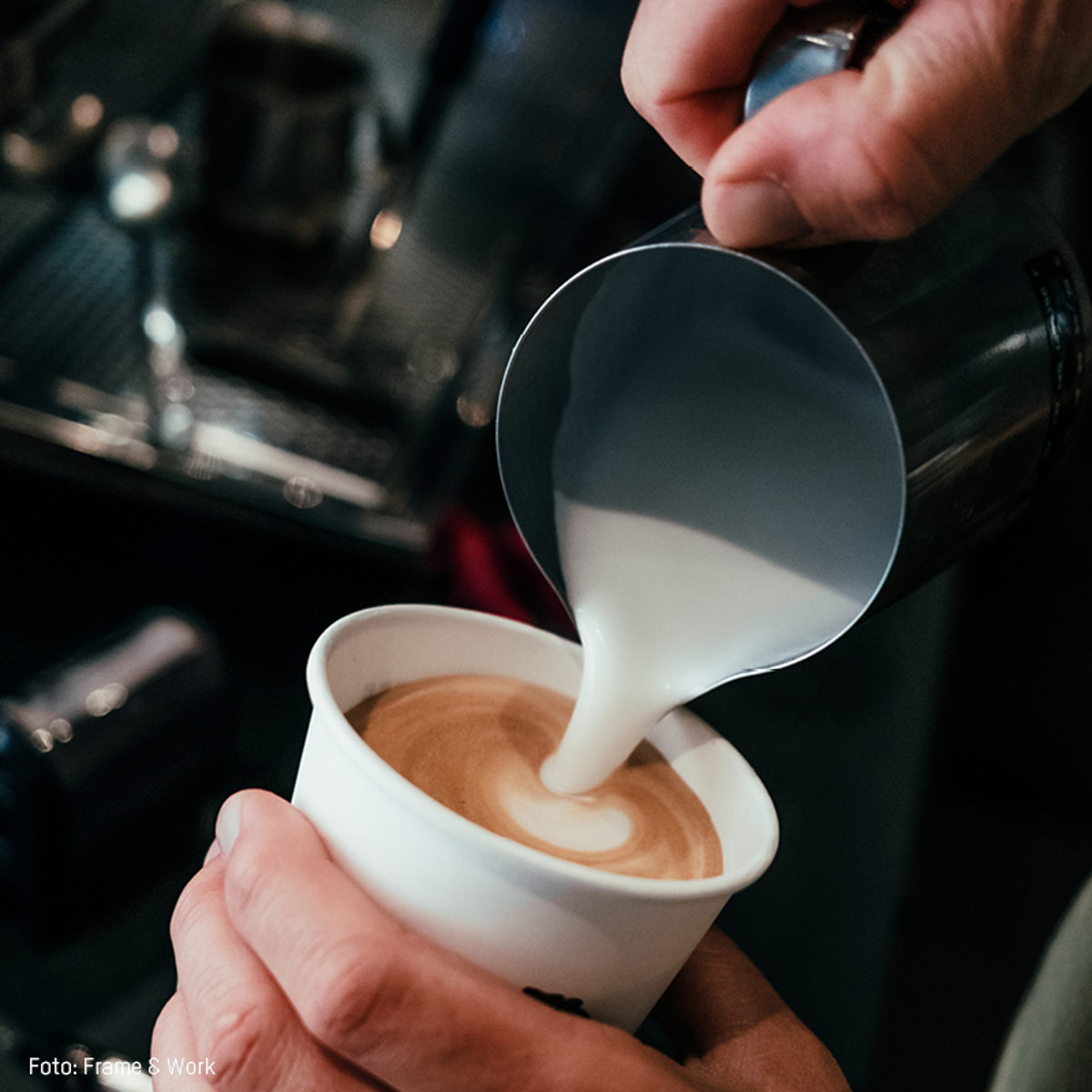 Barista hælder dampet mælk i en kop cappuccino på en kaffebar, der skaber et smukt mønster.