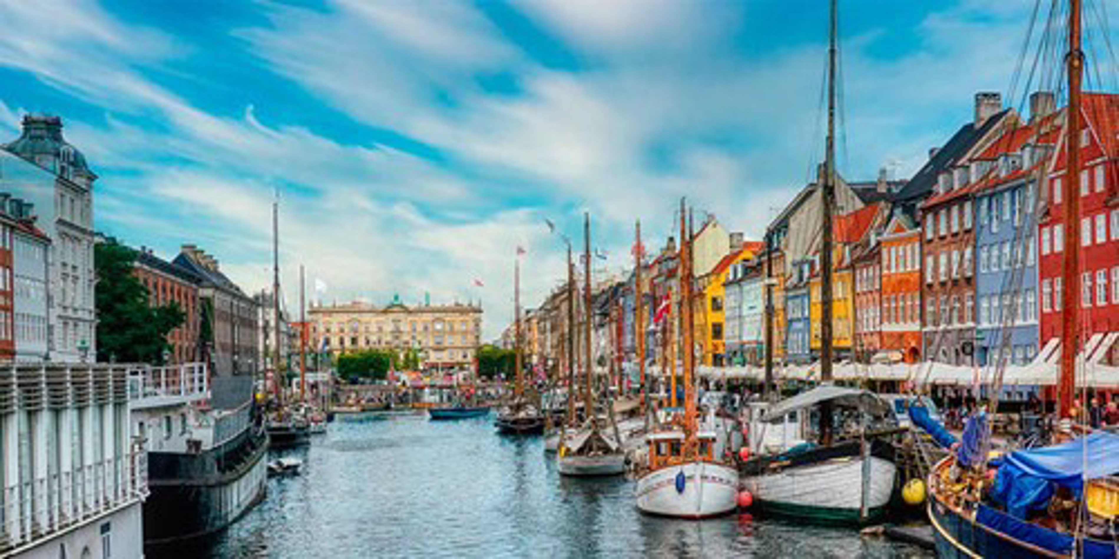 Historiske både ligger til kaj ved Nyhavns farverige bygninger i København under en blå himmel.