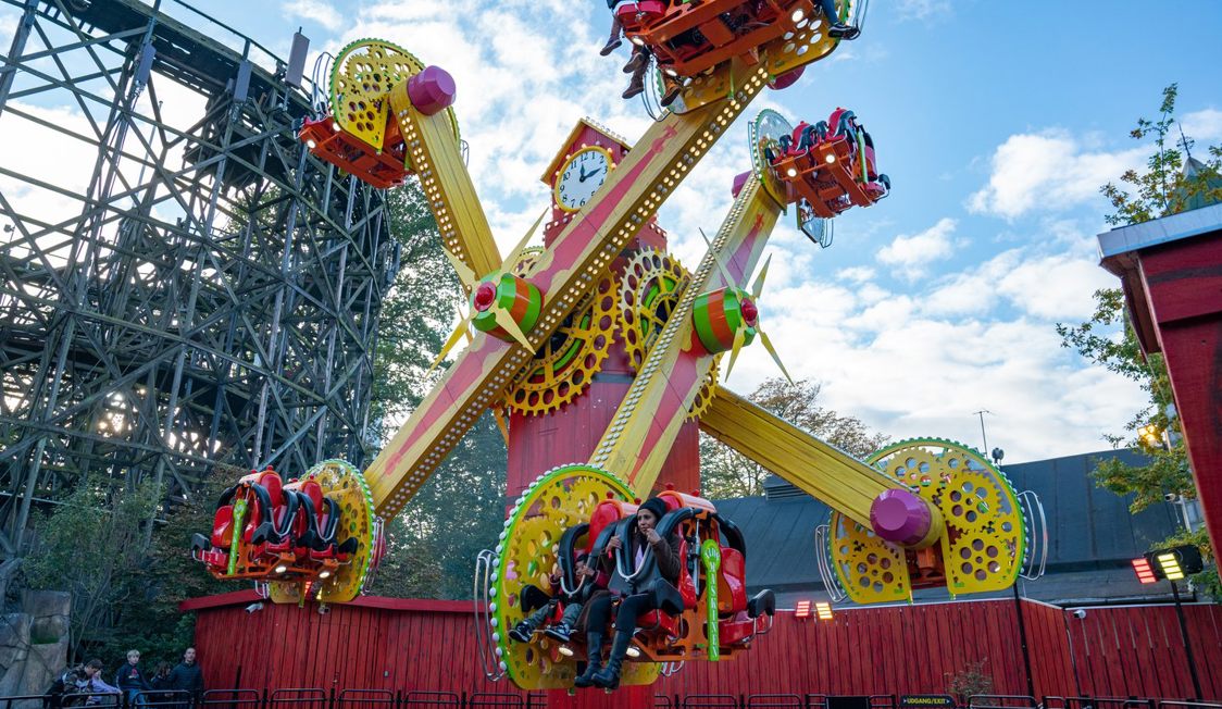 Färgglad karusell i nöjespark svingar gäster upp i luften under en klarblå himmel.