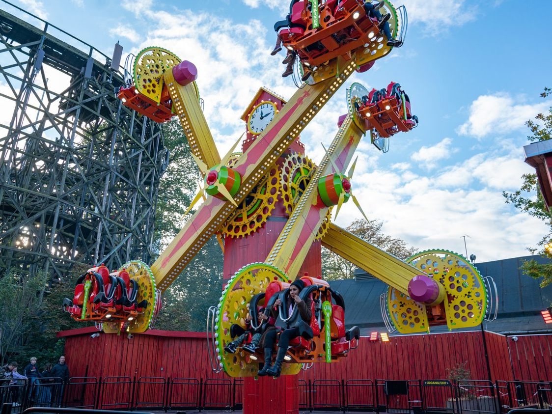 Färgglad karusell i nöjespark svingar gäster upp i luften under en klarblå himmel.
