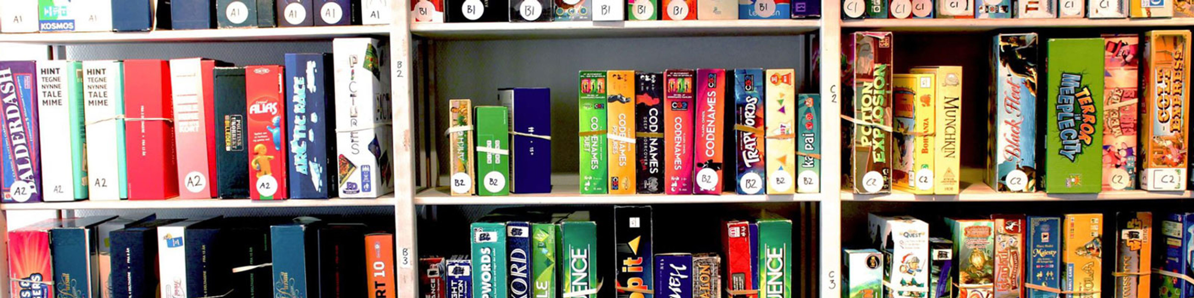 Brætspil stablet på hylder i en butik, forskellige farverige æsker tæt pakket sammen i en række.