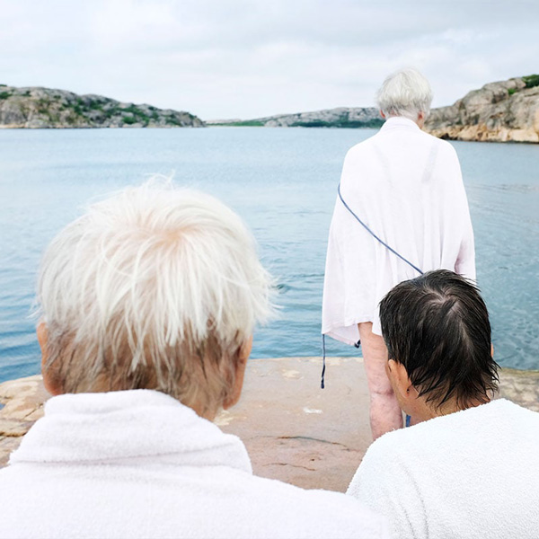 Seniorer iklædt badekåber står ved klippekyst og kigger ud over havet.