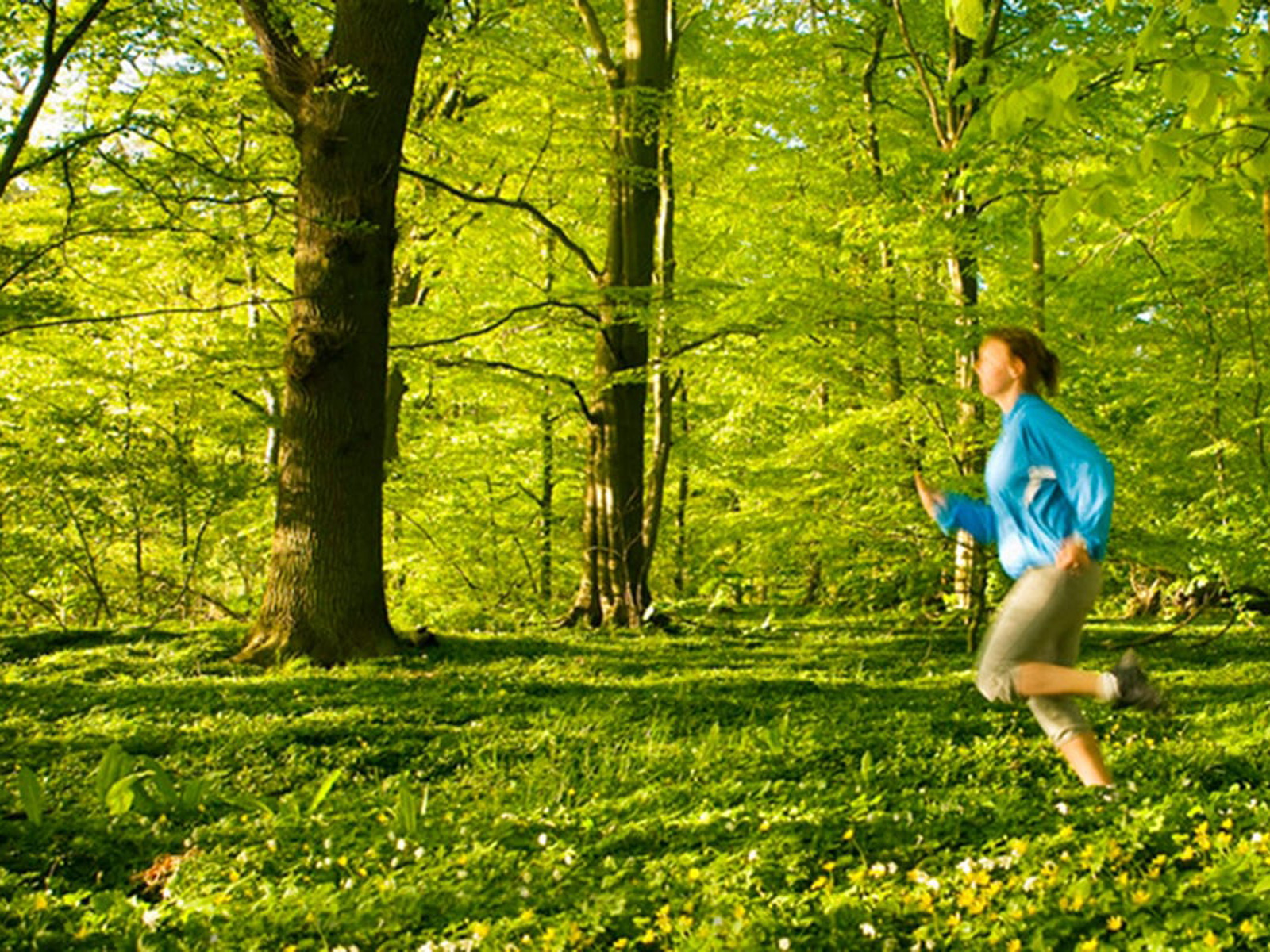 Kvinde løber gennem frodig skov i blåt sportstøj om foråret.