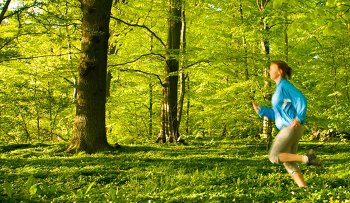 Kvinde løber gennem frodig skov i blåt sportstøj om foråret.