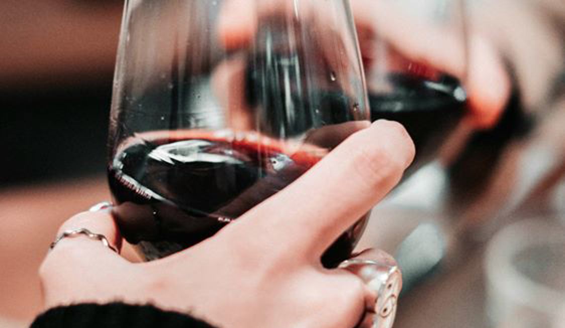 To hænder holder på vinglas med rødvin i tæt opstilling.