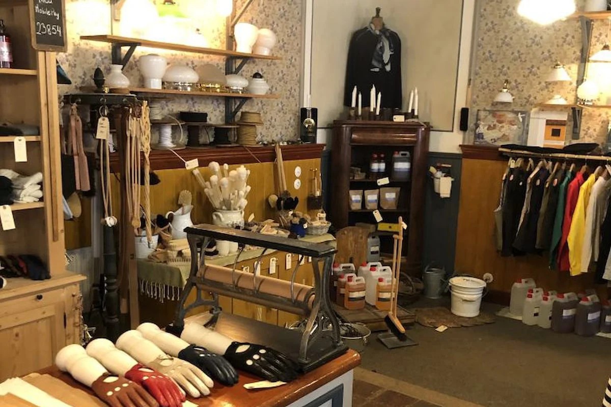 Vintage butik interiör med diverse hushållsartiklar och lakansrullar på ett stationärt stativ.