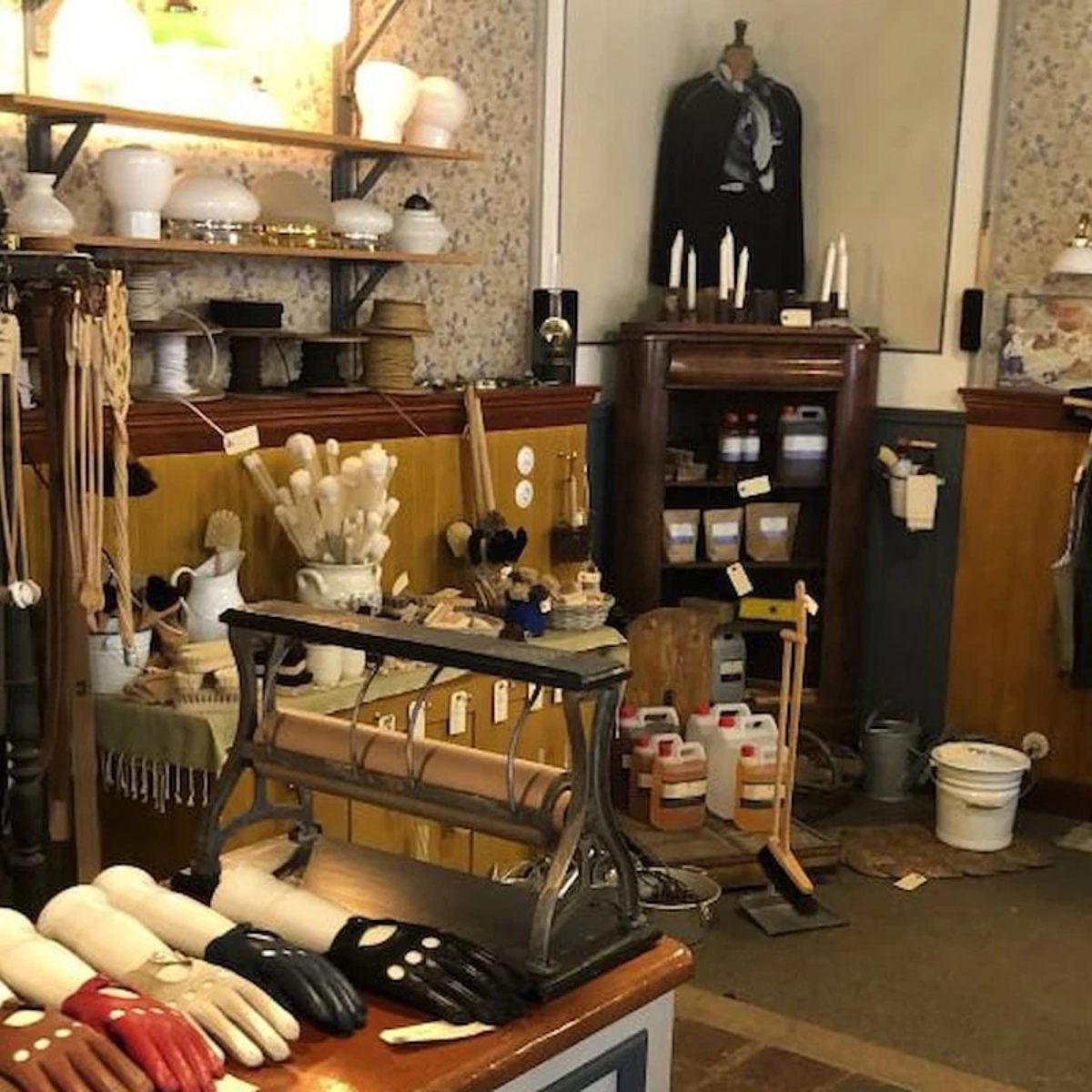 Vintage butik interiör med diverse hushållsartiklar och lakansrullar på ett stationärt stativ.