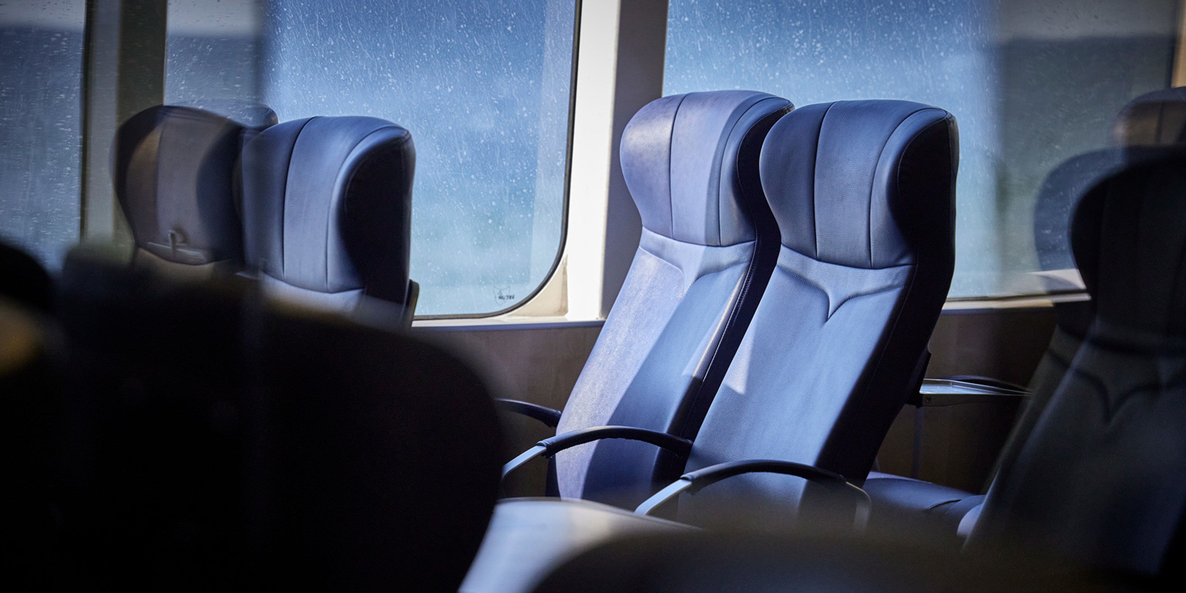 Blå passagersæder ombord på et skib ved siden af et vindspejl med udsigt over det stormfulde hav.