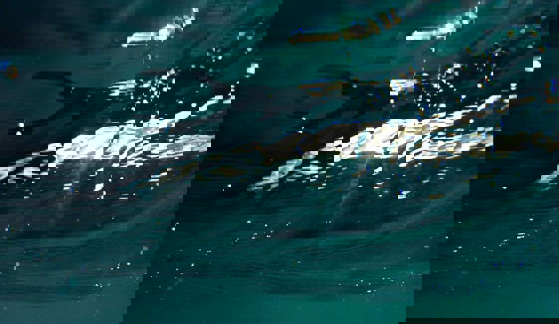 Blått vatten med vågor i närbild där solen skimrar i ytan, vilket skapar en rogivande havsvy.