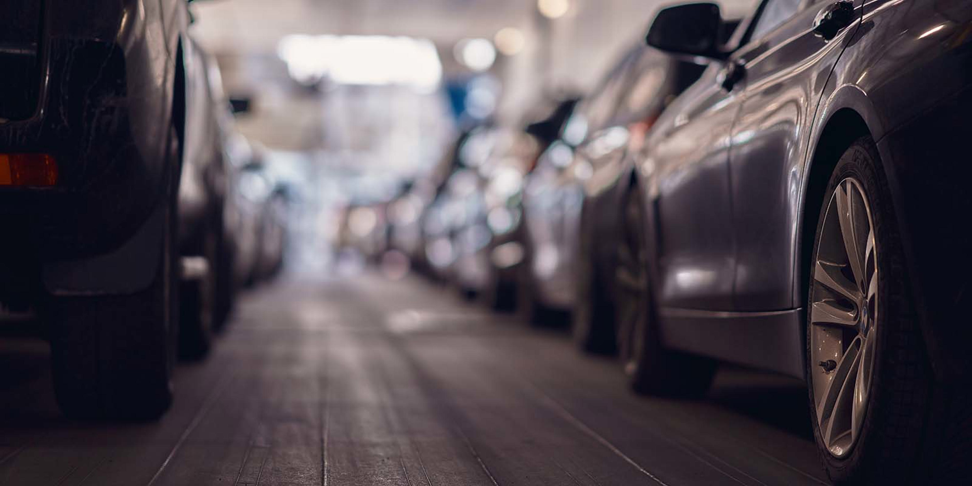 Biler parkeret i en oplyst indendørs garage, set fra lav vinkel ved siden af hjul og refleksioner.