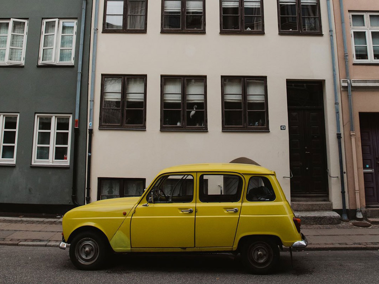 Gul bil parkerad framför ett beige hyreshus i en urban miljö.