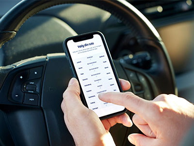 En person navigerer vejretninger på en smartphone i en bil og vælger en rute på touchskærmen.