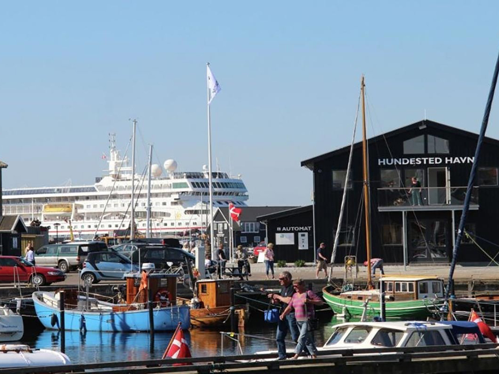 Hundested Hamn med brygghus och småbåtar, en färja syns i bakgrunden under en klar himmel.