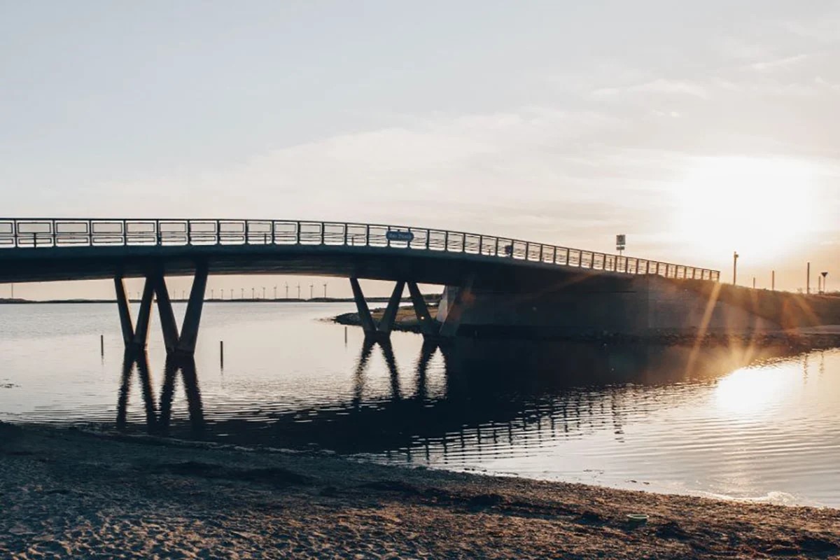 Bro över vatten vid solnedgång, Amager Strandbro  med solens strålar som lyser upp bron och speglas i vattnet.