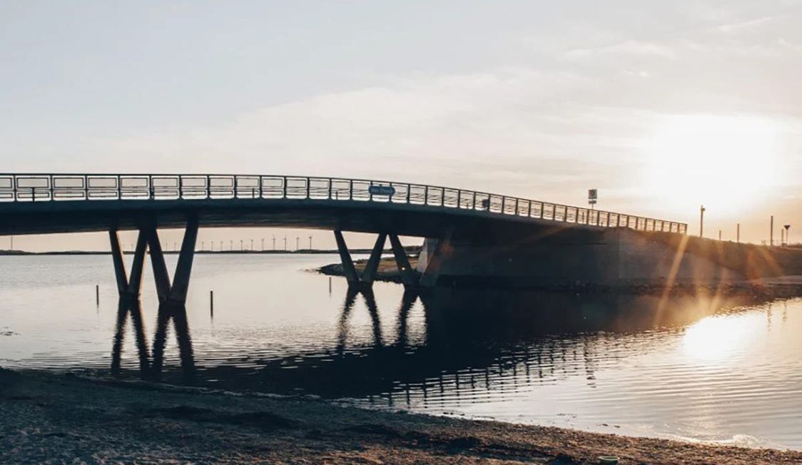 Bro över vatten vid solnedgång, Amager Strandbro med solens strålar som lyser upp bron och speglas i vattnet.