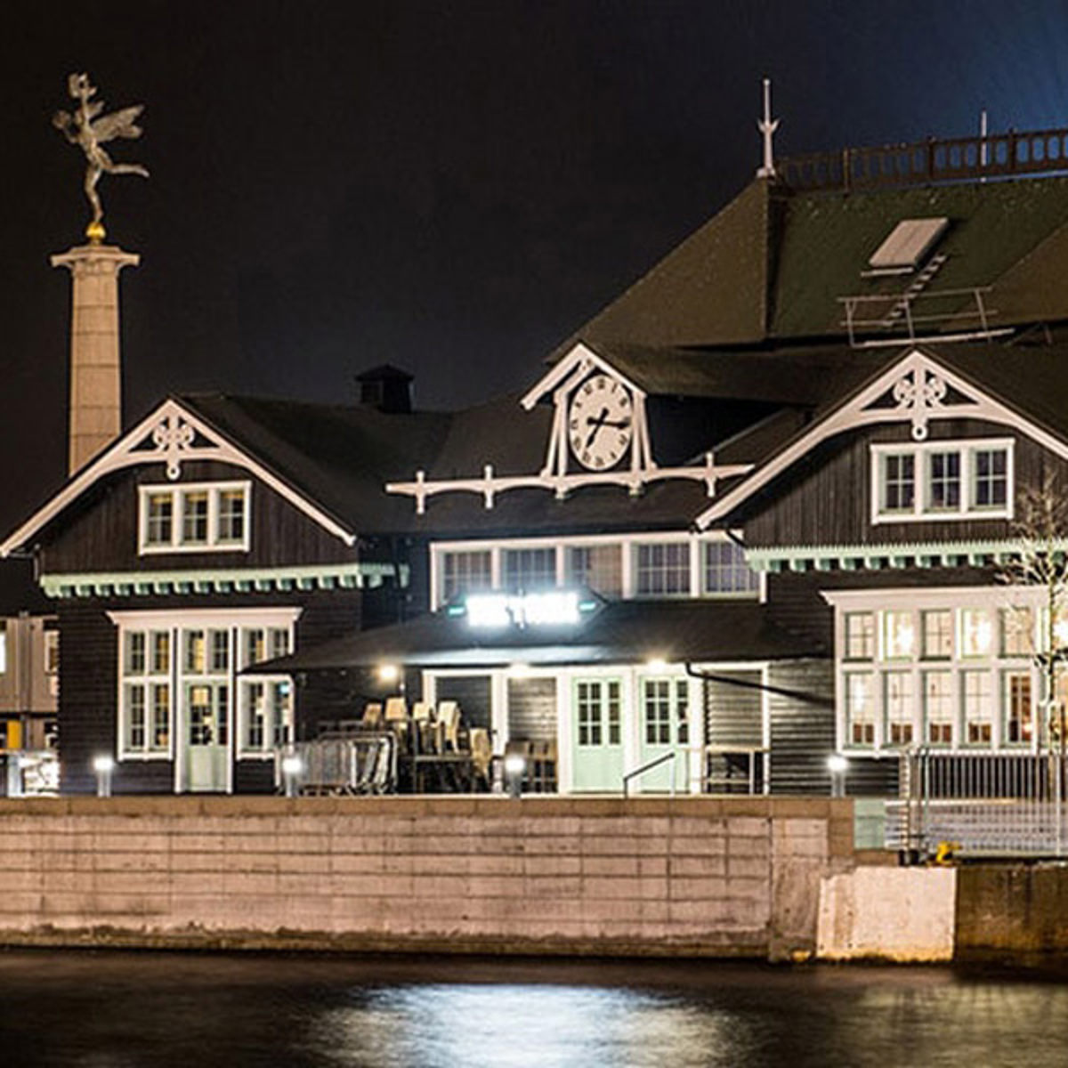 Historisk bygning med ur på facaden oplyst om natten, set i fugleperspektiv.