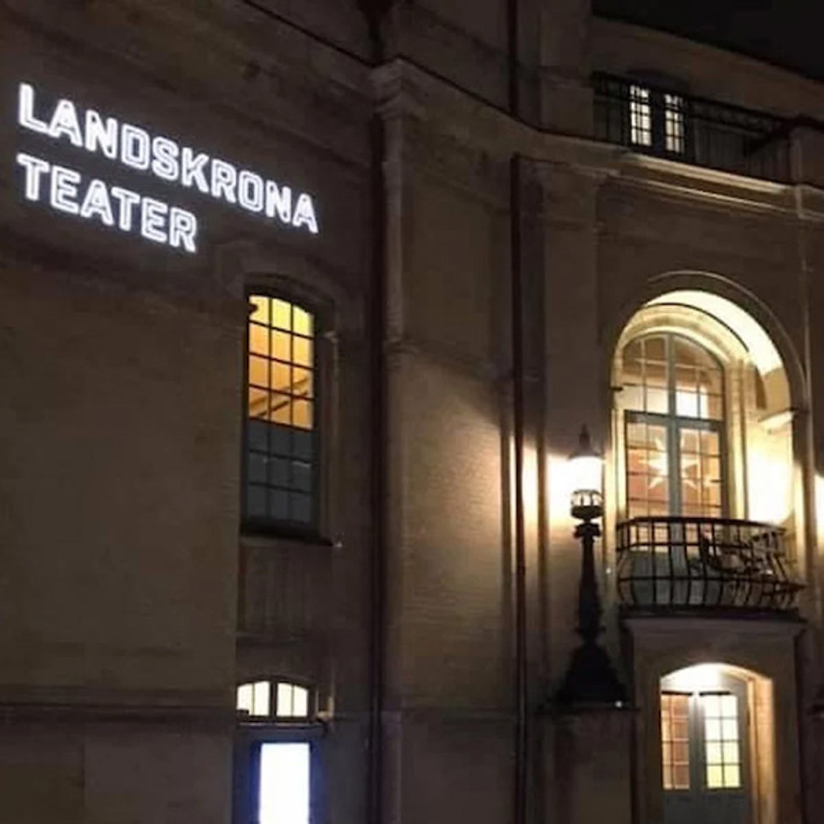Landskrona Teater oplyst facade om natten med klassisk belysning og vinduesbalkon.