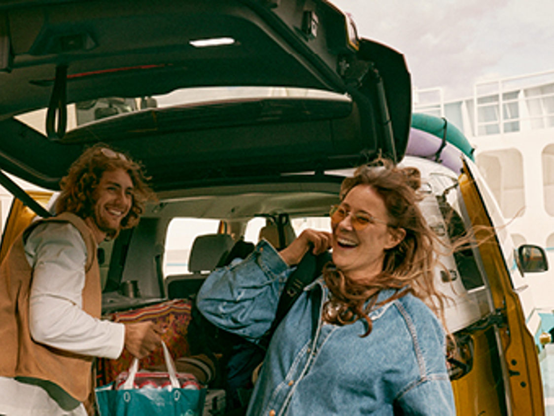 Par på campingtur pakker bagage i bilens bagagerum med latter og glæde.