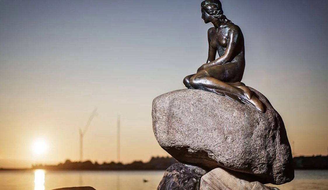 Skulpturen "Den lille havfrue" sitter på en sten vid vattnet under solnedgången.