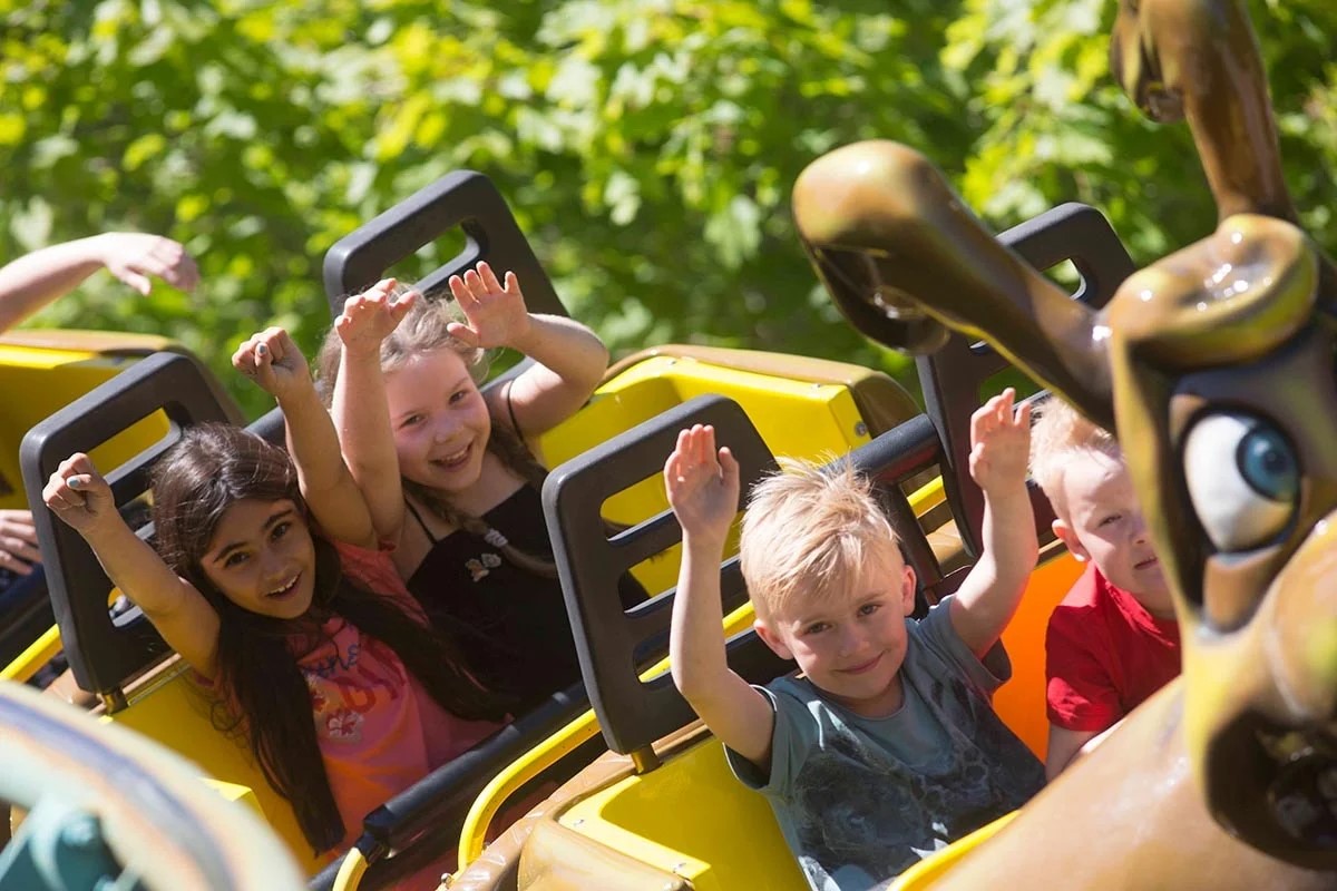 Barn åker bergodalbana på Bonbonland med händerna upp i luften och ser glada ut.