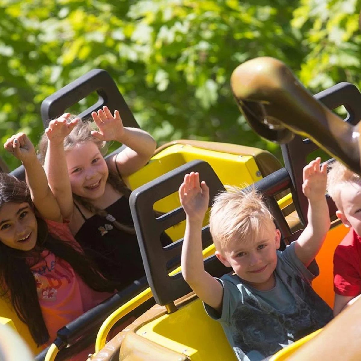 Barn åker bergodalbana på Bonbonland med händerna upp i luften och ser glada ut.
