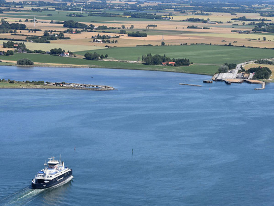 Fugleperspektiv af Langelandslinjen på åbent hav med retning mod marker og strand.