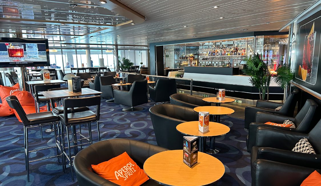 Moderne bar og lounge med komfortable læderstole og borde, stilfuldt interiør og Aperol Spritz dekorationer.