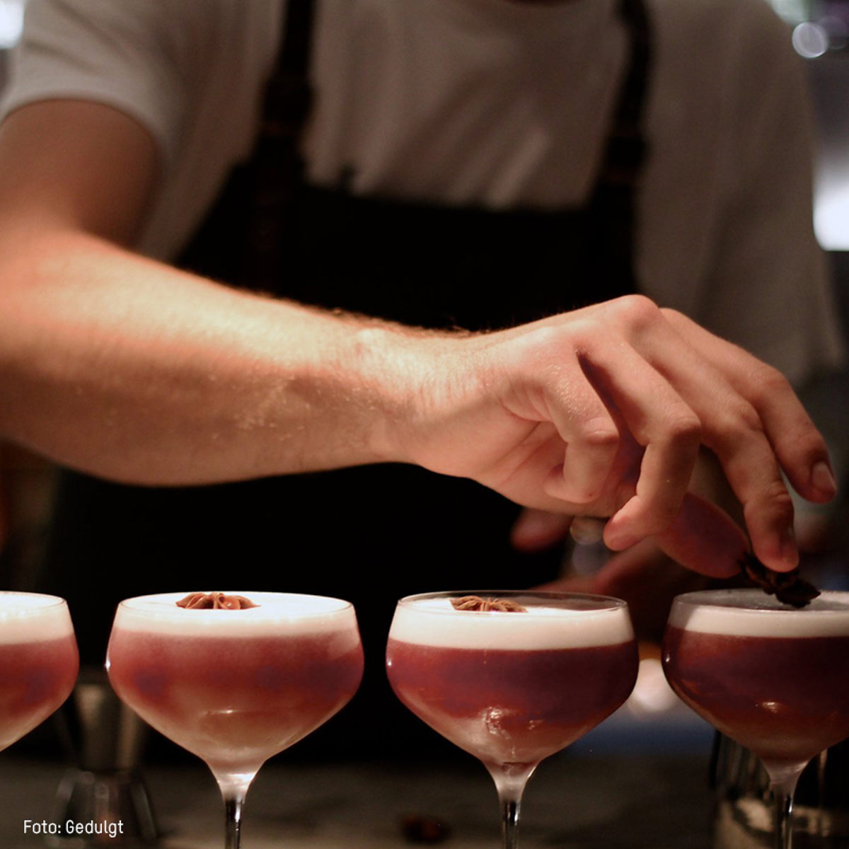 Bartender pynter cocktailglas med krydderi på bar.