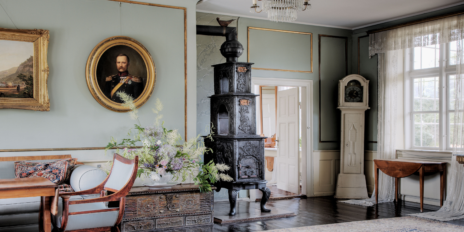 Antik sort kakkelovn med indviklede detaljer står i stilfuld stue mellem portrætmalerier og blomstervase.