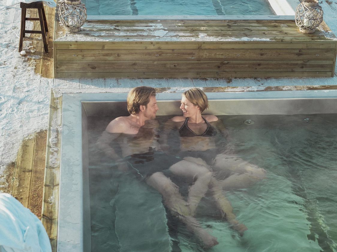 Par nyder varmt udendørs spabad omgivet af sne fra oven.