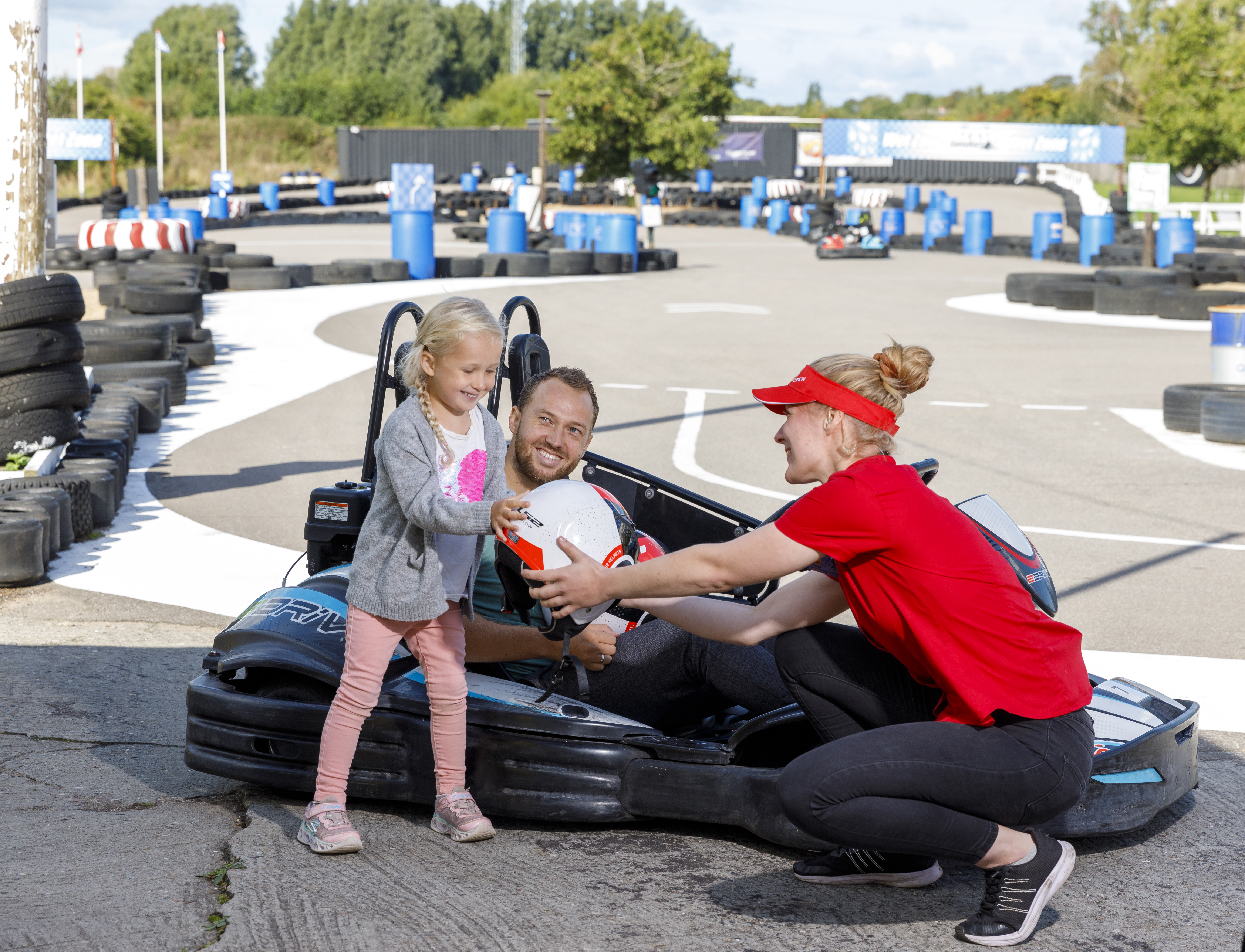 Familjen  kör gokart med Lars och Cecilia på en bana, njuter av en solig dag med hjälm och utekul.