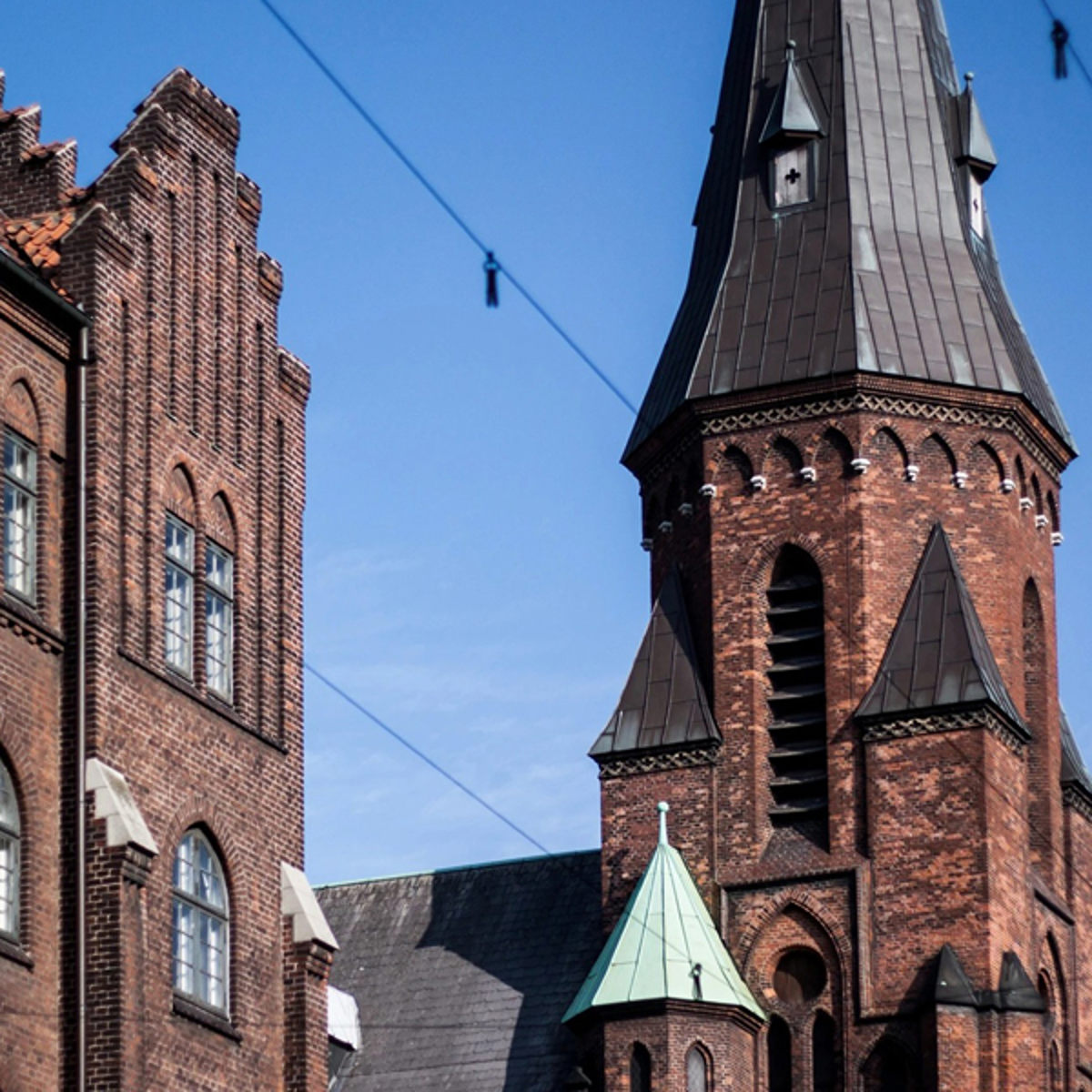 Gammel murstenskirke med højt spir under en klar blå himmel i centralt bymiljø.