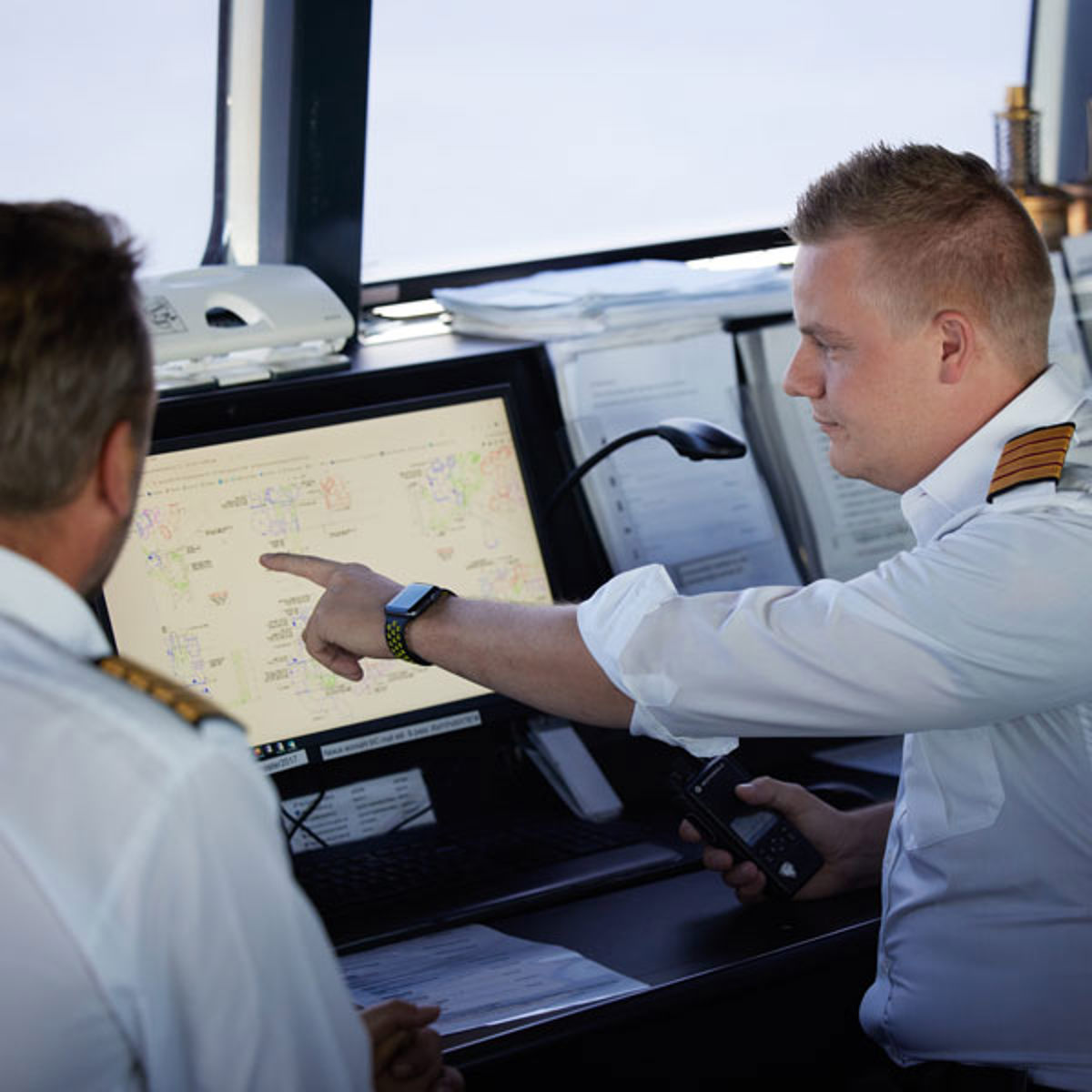 To besætningsmedlemmer diskuterer navigationskort på computer i skibets kontrolrum.