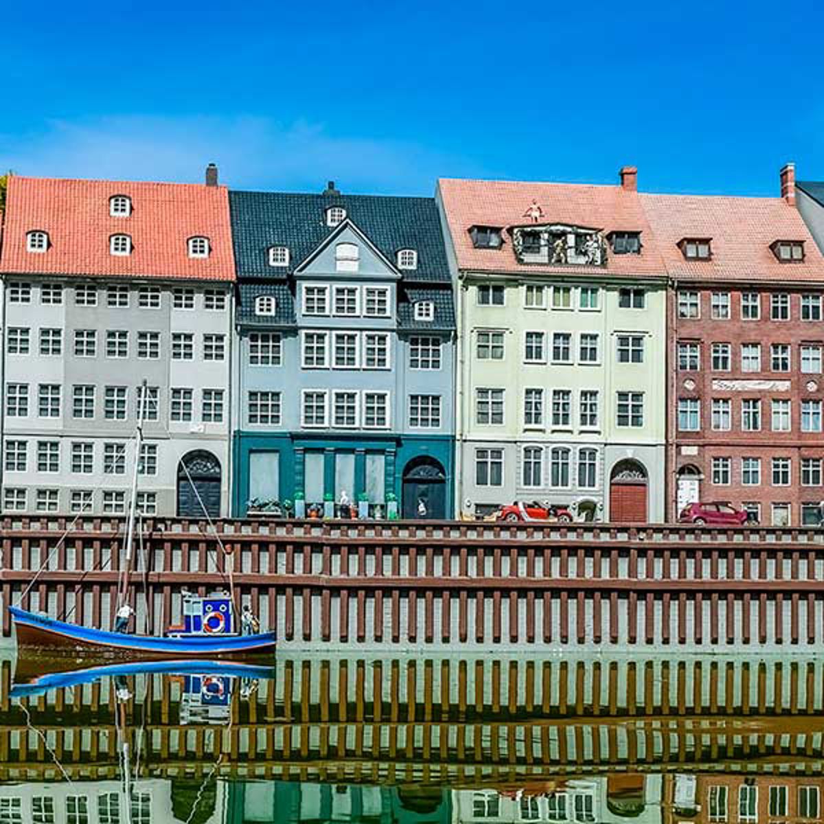 Farverige historiske bygninger langs kanalen i Nyhavn, København, afspejlet i vandet en solrig dag.