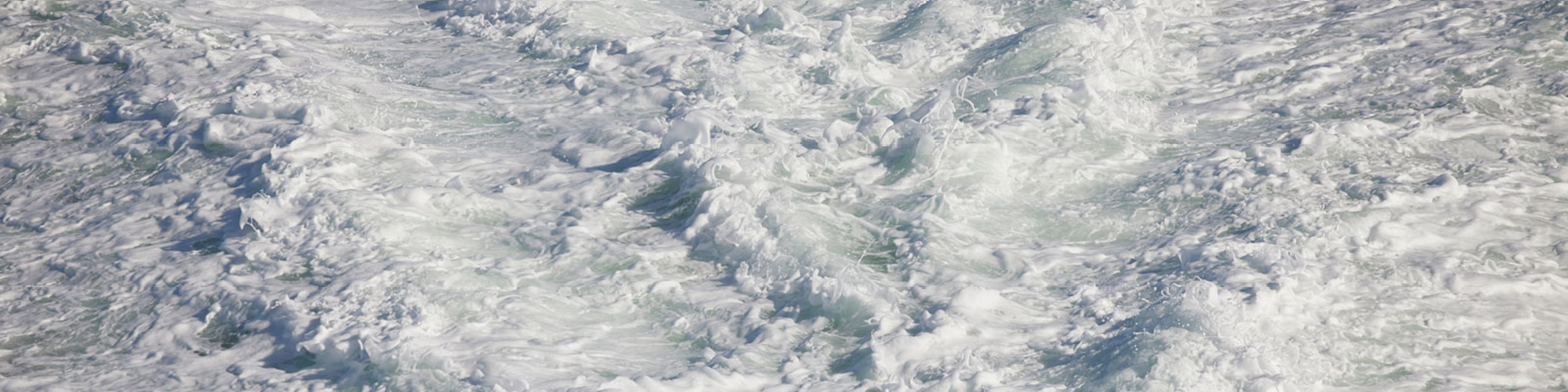 Foamy sea spray from a busy ferry, with frothy waves and white splashing water viewed from above.