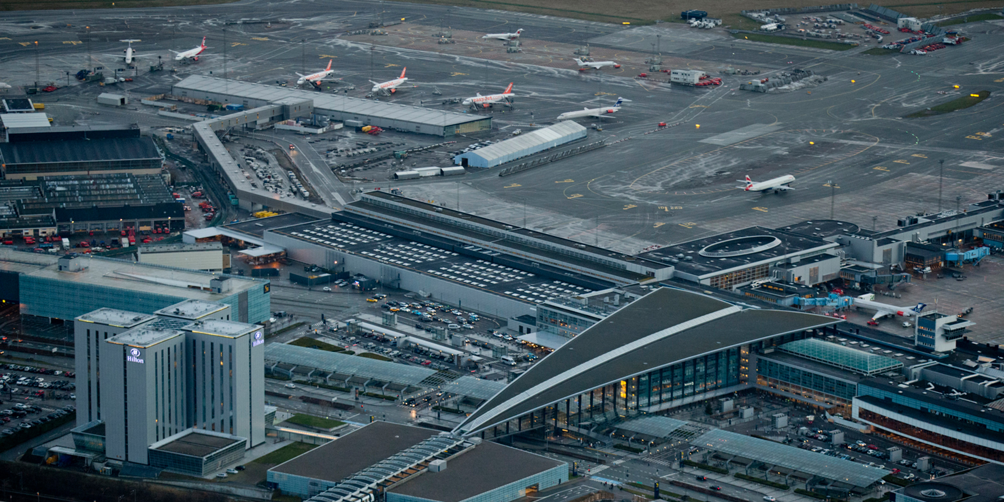 Luftfoto af Københavns Lufthavn med terminaler og parkerede fly samt lufthavnshotel i forgrunden.
