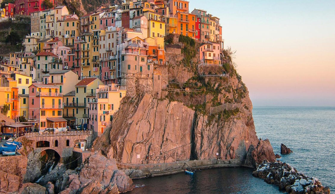 Färgglada hus i Medelhavet V2 vid kustklippa i solnedgångsljus.