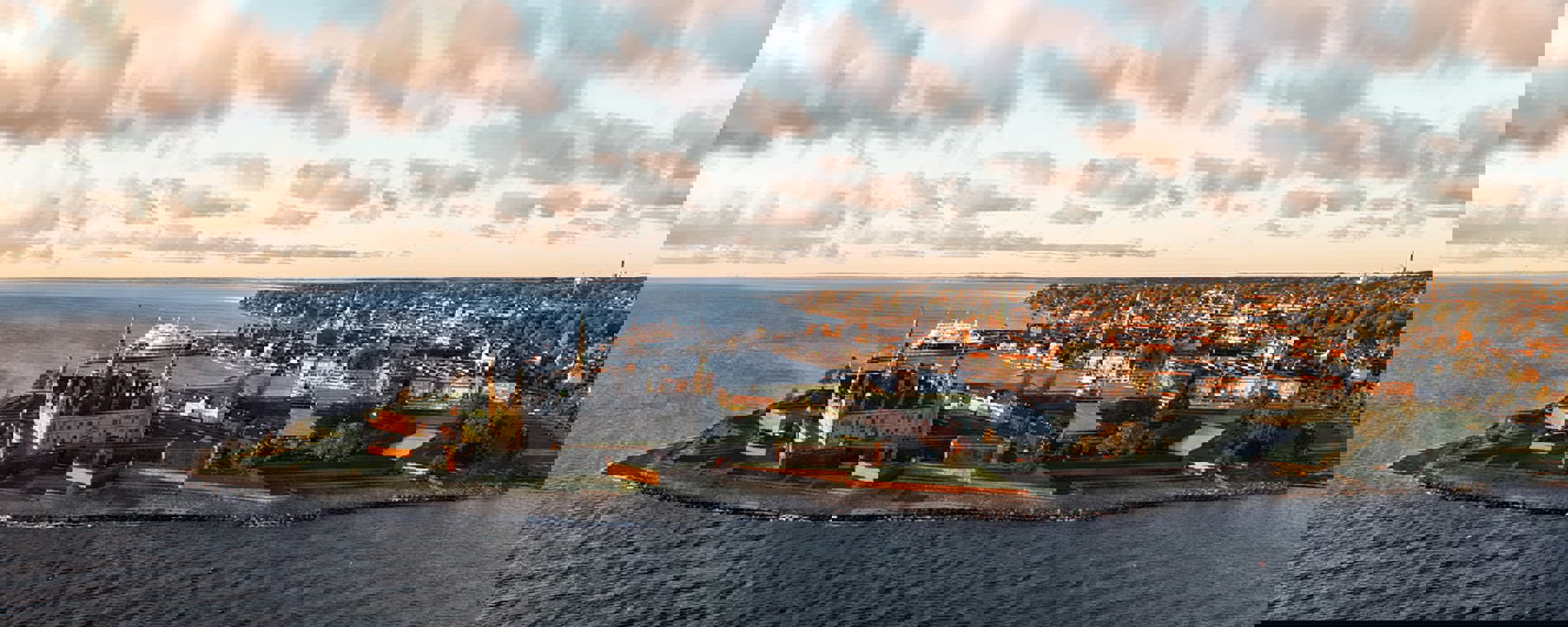 Luftfoto af Helsingør ses i aftensolens stråler omringet af havet.