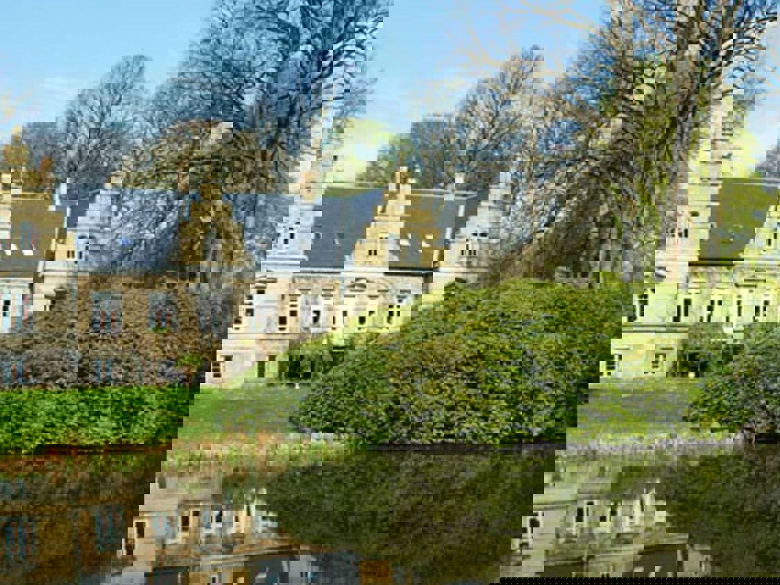 Nivaagaard med buskar och vatten i förgrunden.