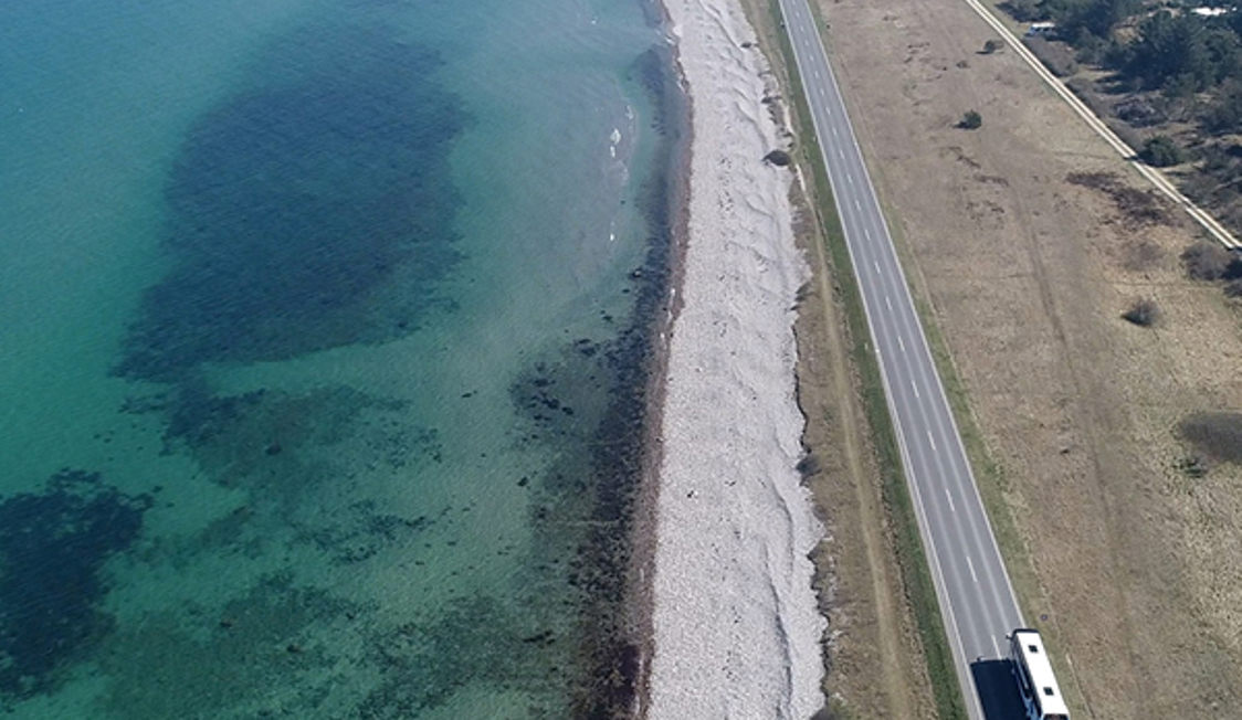 Bus kører langs kystvejen med udsigt over det klare, blå hav i fugleperspektiv.