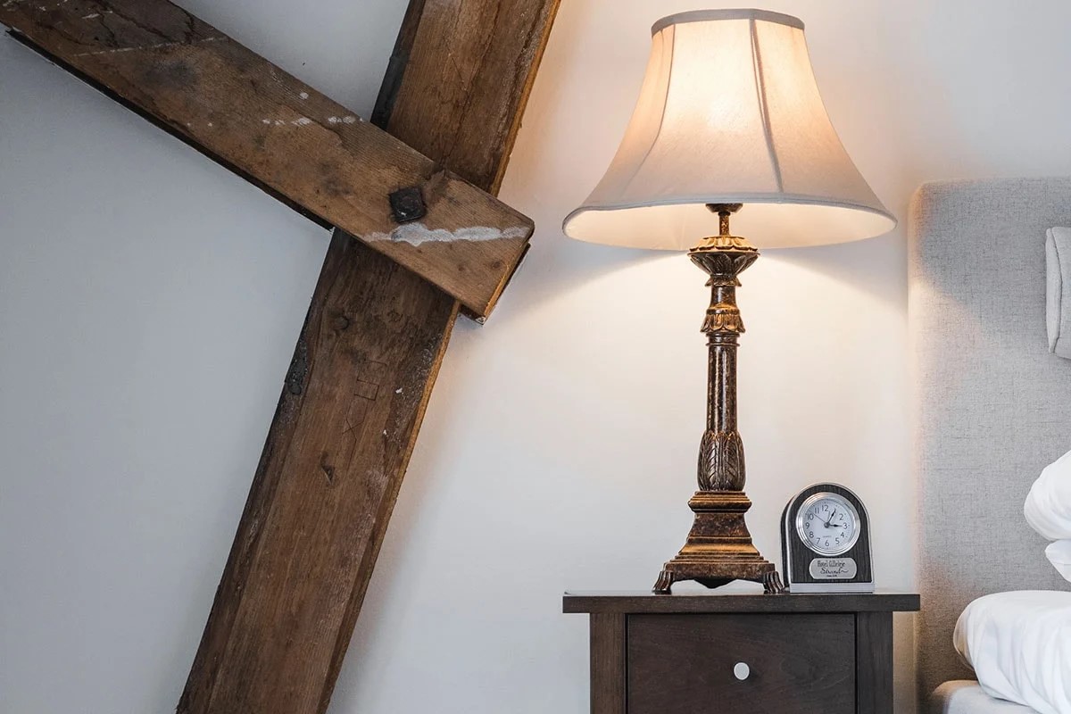 Gilleleje Strand Hotel sängbord med klassisk lampa och klocka på träyta, bredvid en träbalk.