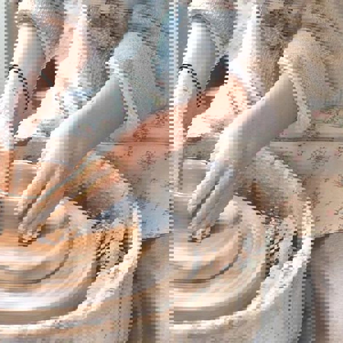 En kvinna sitter och spinner lera.