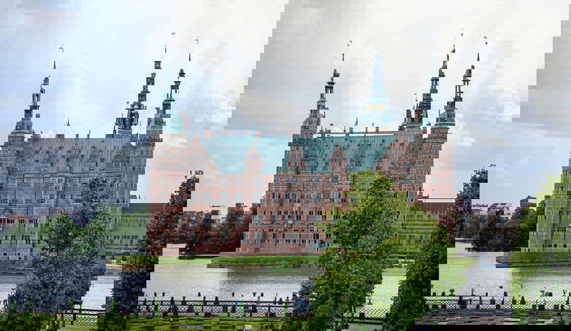 Frederiksborg i solsken omgiven av spegelblankt vatten.