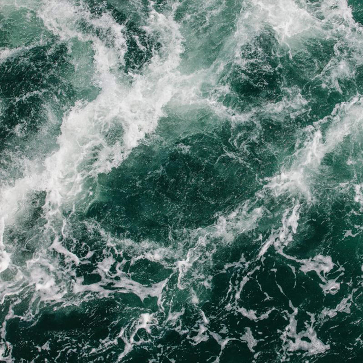 Havvand med skum på overfladen set ovenfra, viser turbulente bølger og hvirvler i dyb grønt.