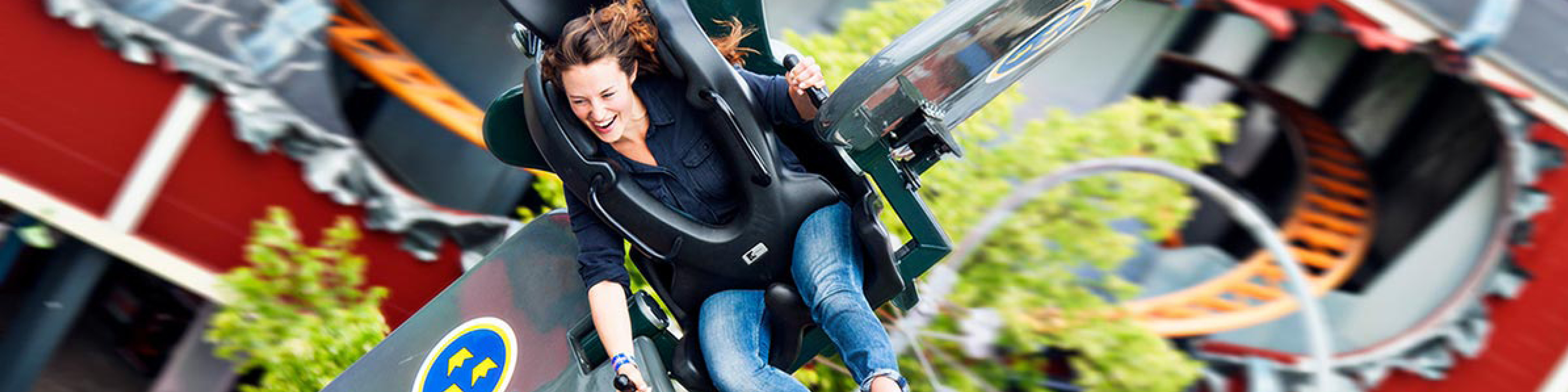 Kvinna njuter av spännande berg-och-dalbana, ler och höjer händerna i luften i nöjespark.