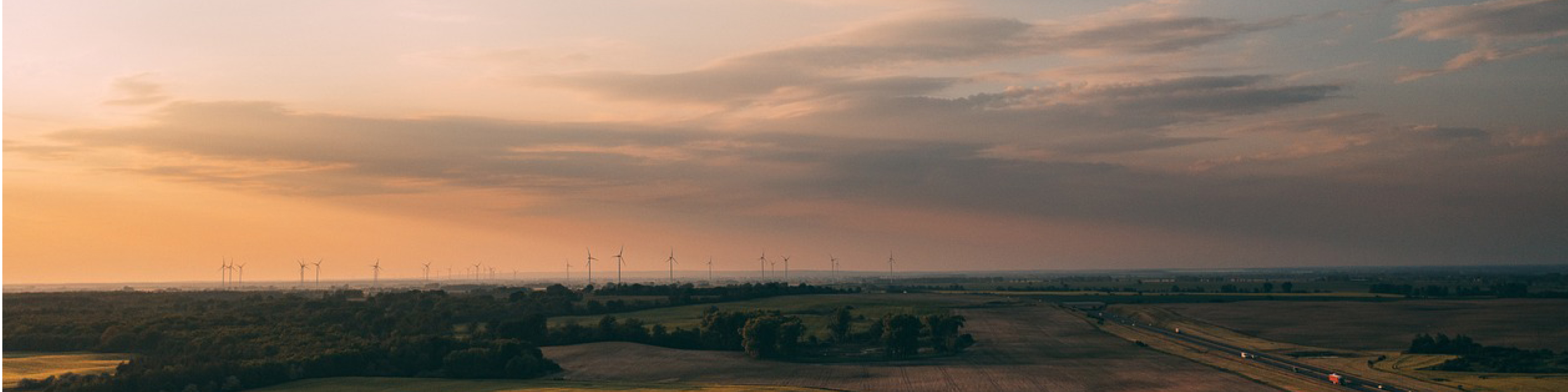 Vindkraftverk på öppen mark vid solnedgång i fågelperspektiv.