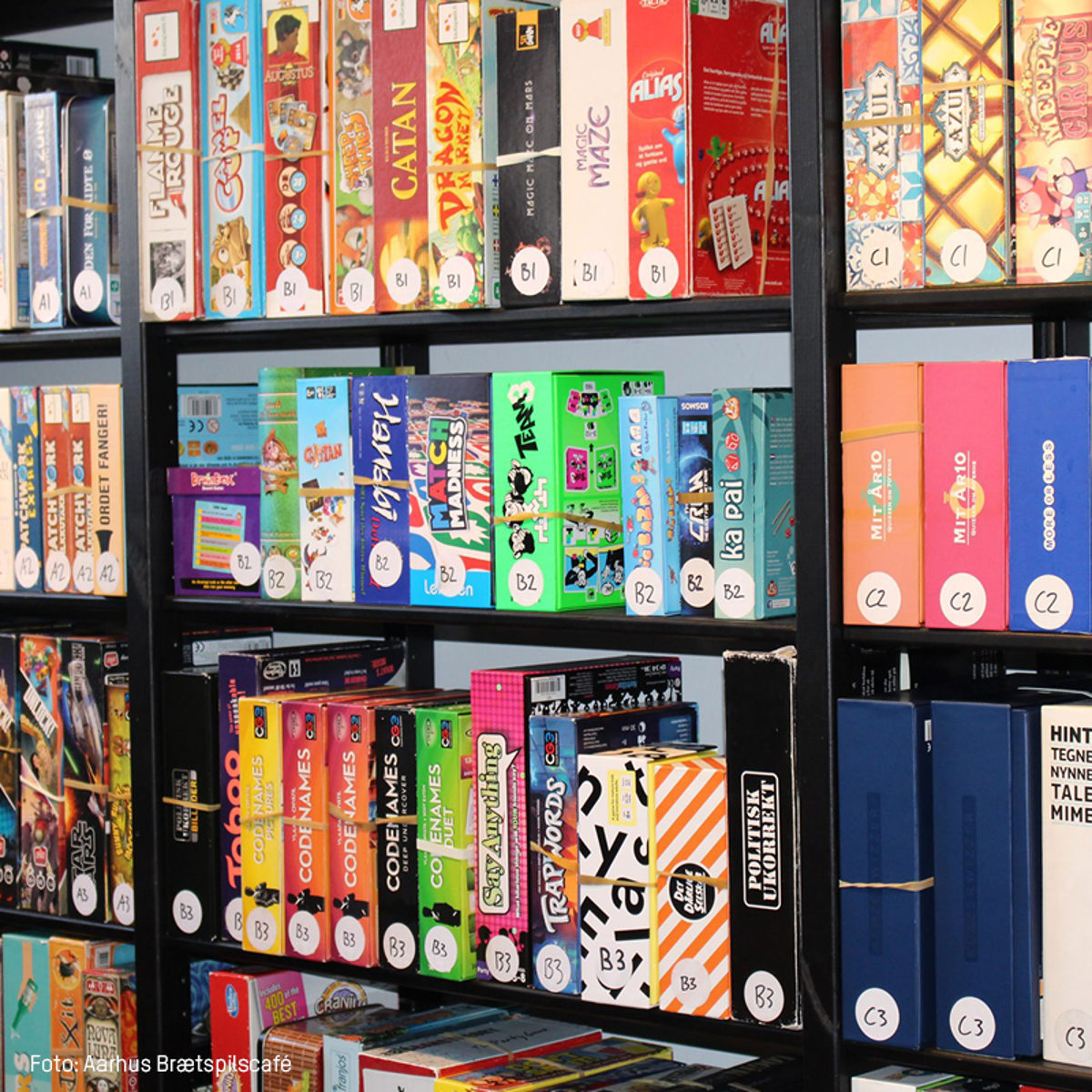 Brætspil i farverige kasser står på hylder i et spilbibliotek i Aarhus Brætspilscafé.