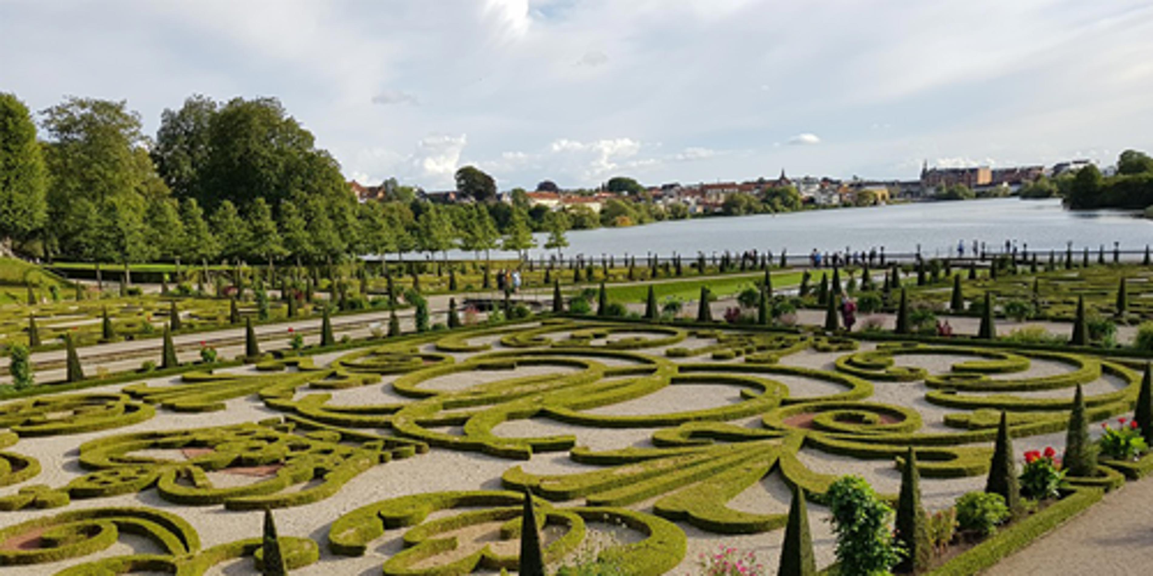 Symmetrisk barokhave med snoede hække ved søen på en solrig dag i Danmark.
