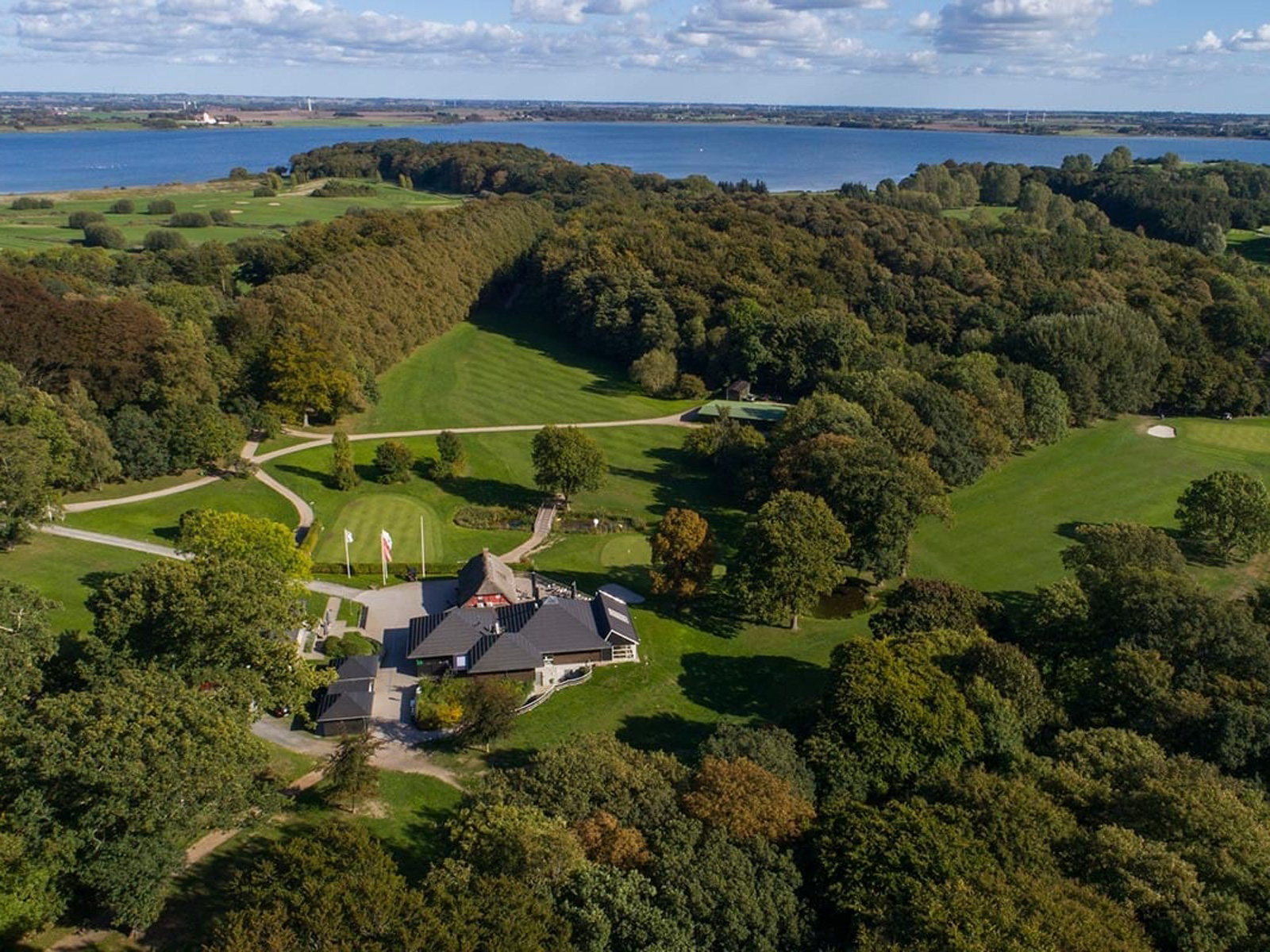 Flygfoto över Korsør Golfklubb med böljande gröna fairways och omgivande skogar vid vattnet.